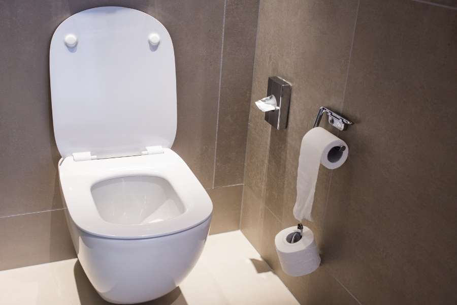 Abattant de WC blanc ouvert sur des toilettes suspendues modernes dans une salle de bains carrelée de gris