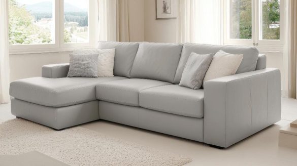 Grand canapé d'angle en cuir gris clair avec méridienne à gauche et coussins décoratifs dans un salon lumineux.
