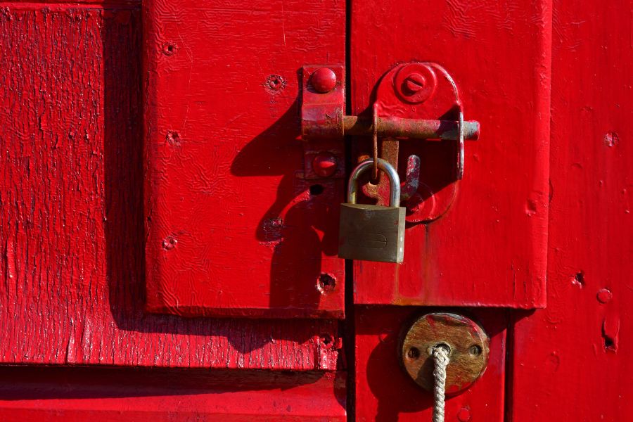 Un cadenas en laiton fixé sur un loquet métallique monté sur une porte en bois rouge, illustrant comment choisir une serrure de sécurité pour un abri de jardin ou un cabanon.